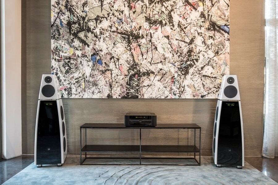 High-end audio speakers as part of a home sound setup with artwork on a wall and a table in between them.