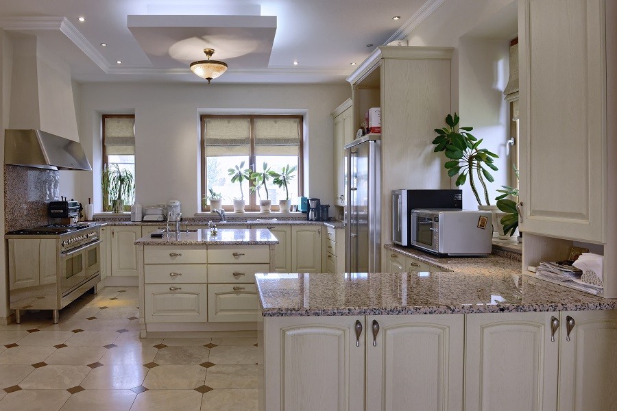 Photo of a beautiful white kitchen with recessed lighting and motorized shades on the windows.