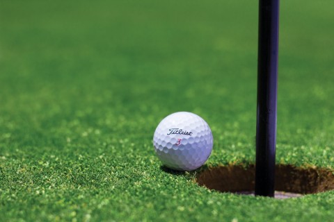 Golf ball sitting on a green right next to a hole. 