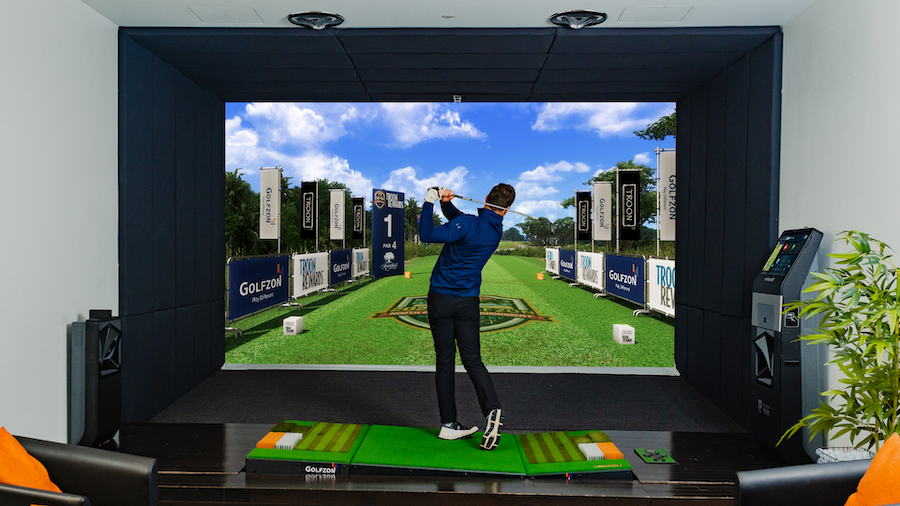 Golfzon simulator in a garage. Controls and golf clubs stand next to the putting zone.